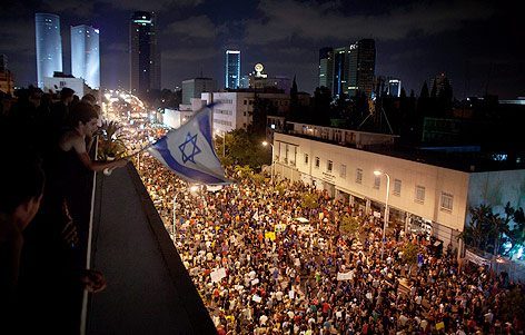 Mann beobachtet mit Israel-Fahne in der Hand die protestierende Menschenmasse auf der Straße in Tel-Aviv