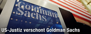 Schriftzug von Goldman Sachs mit amerikanischer Flagge im Hintergrund