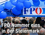 Zuschauer vor FPÖ-Logo und blauen Luftballons