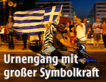 Frau und Mann fahren auf einem Motorrad und schwenken die griechische Fahne
