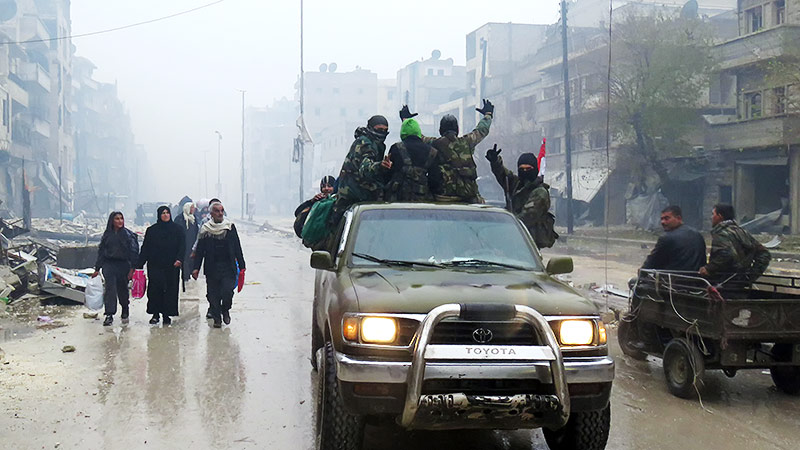 Zivilisten auf einer Straße in Aleppo, daneben jubelnde Regimetruppen