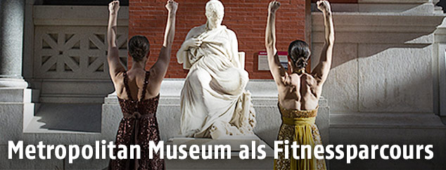 Zwei Frauen strecken ihre Arme vor einer Statue